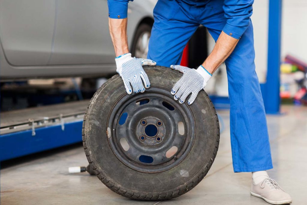 mechanic with wheel tire at car workshop